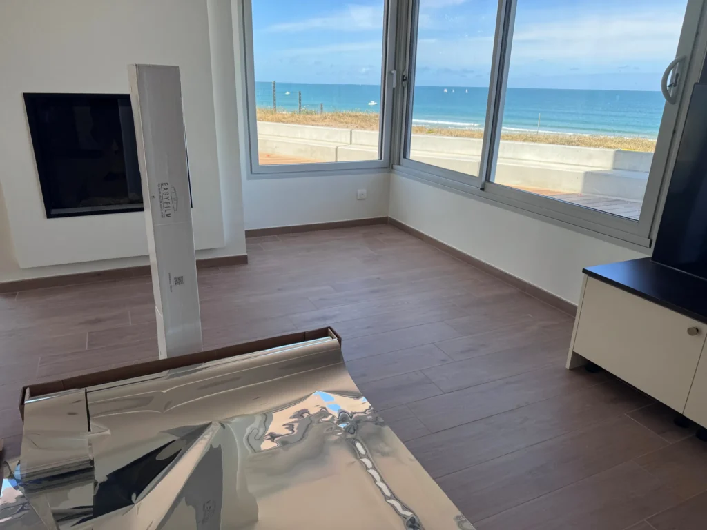 Rouleau de film miroir Easy Film prêt à poser dans le séjour d’une maison face à la mer, avec vue sur le large préservée